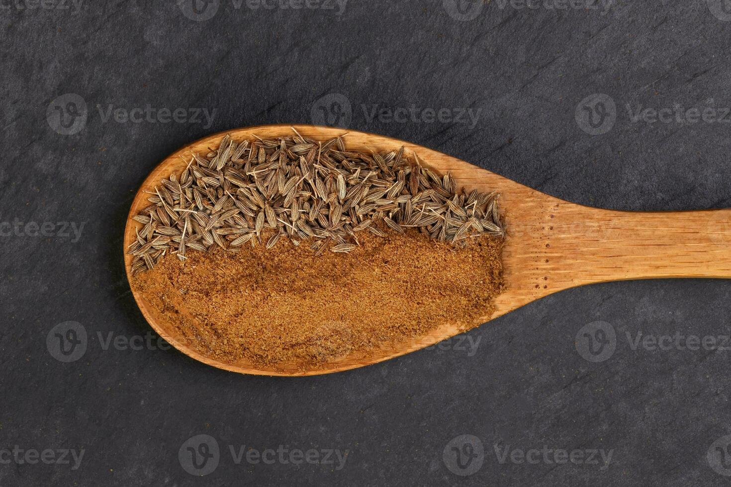 Cumin spice whole powder wooden spoon on black slate background photo