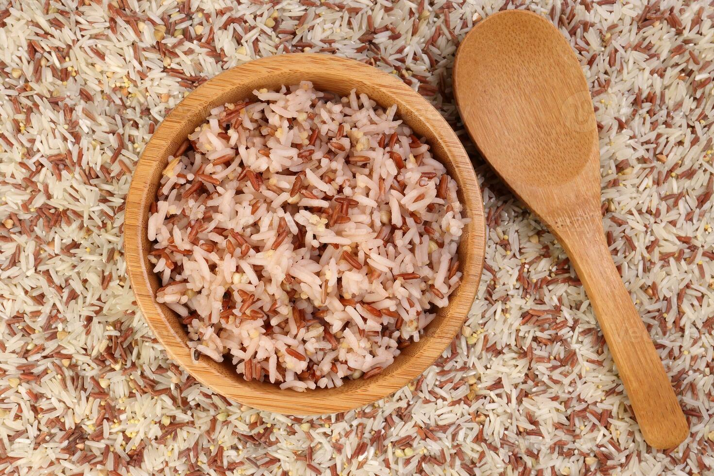 Cooked and raw mixed low glycaemic index healthy rice grain basmati millet buckwheat red rice in wooden bowl spoon bed of rice over white background photo