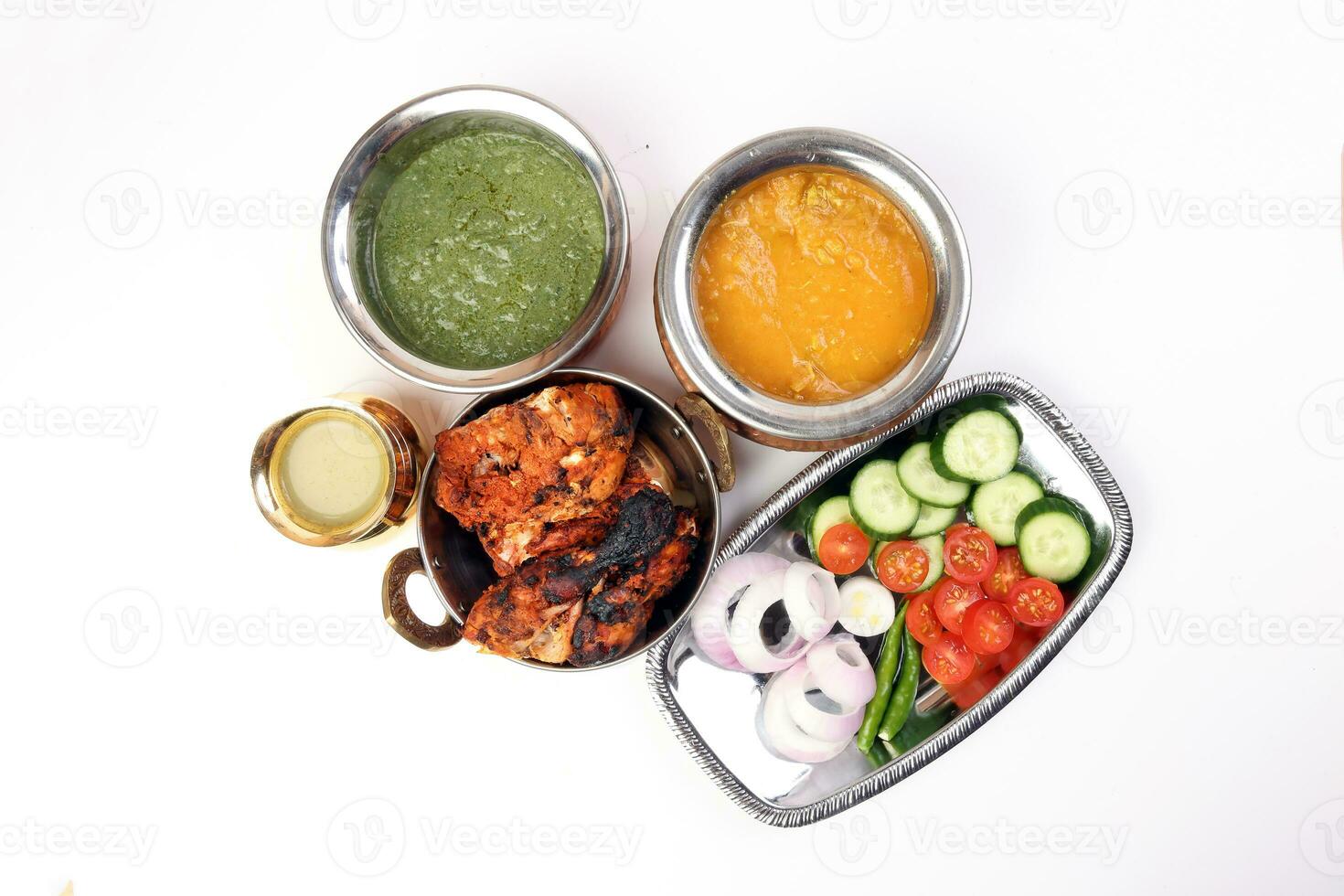 Spicy red Chicken grilled tikka tandoori nan bread green spinach curry yogurt sauce dal tomato cucumber onion salad set in metal stainless steel brass copper pot on white background photo