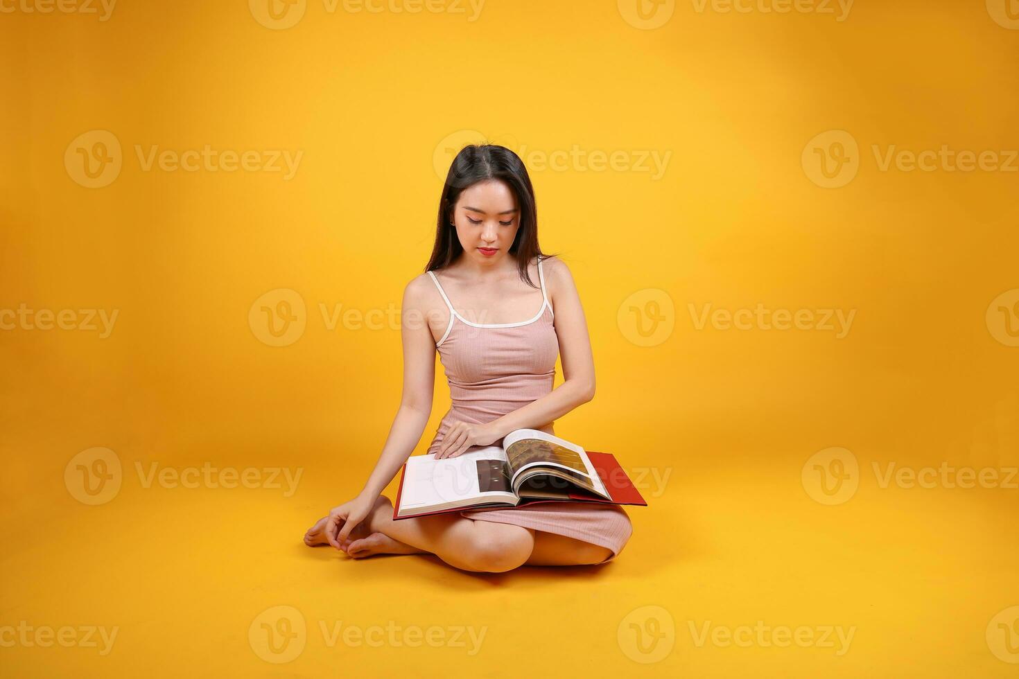 Beautiful young south east Asian woman sit down on floor yellow orange color background read study book magazine pose fashion style elegant beauty mood photo