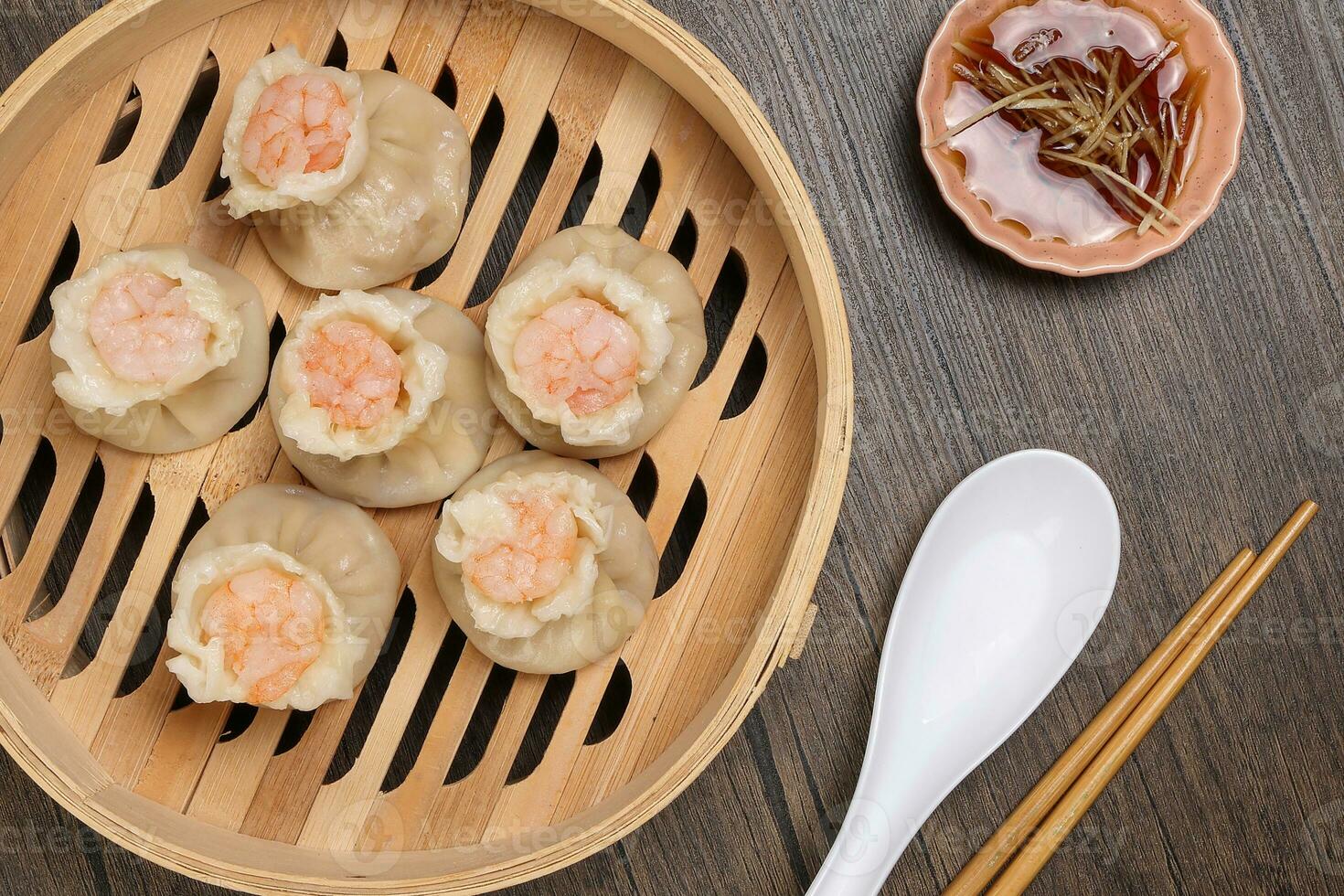 Prawn shrimp shaomai dim sum dumpling in bamboo steamer sauce chopsticks soup soon on rustic wood background photo