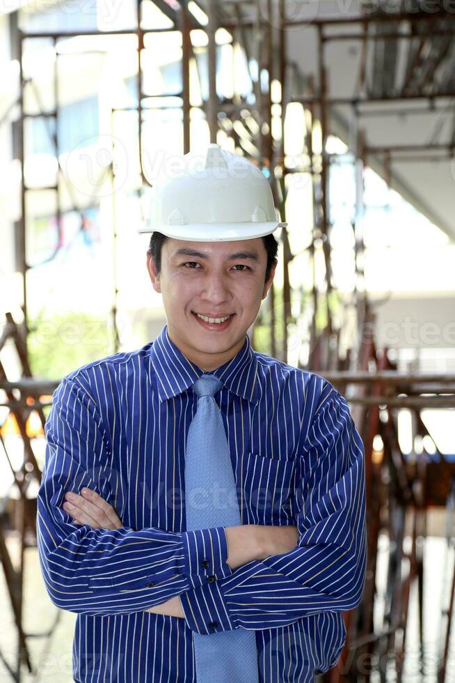South East Asian young Malay Chinese man wearing white yellow safety helmet tie look at camera smile cross hand photo