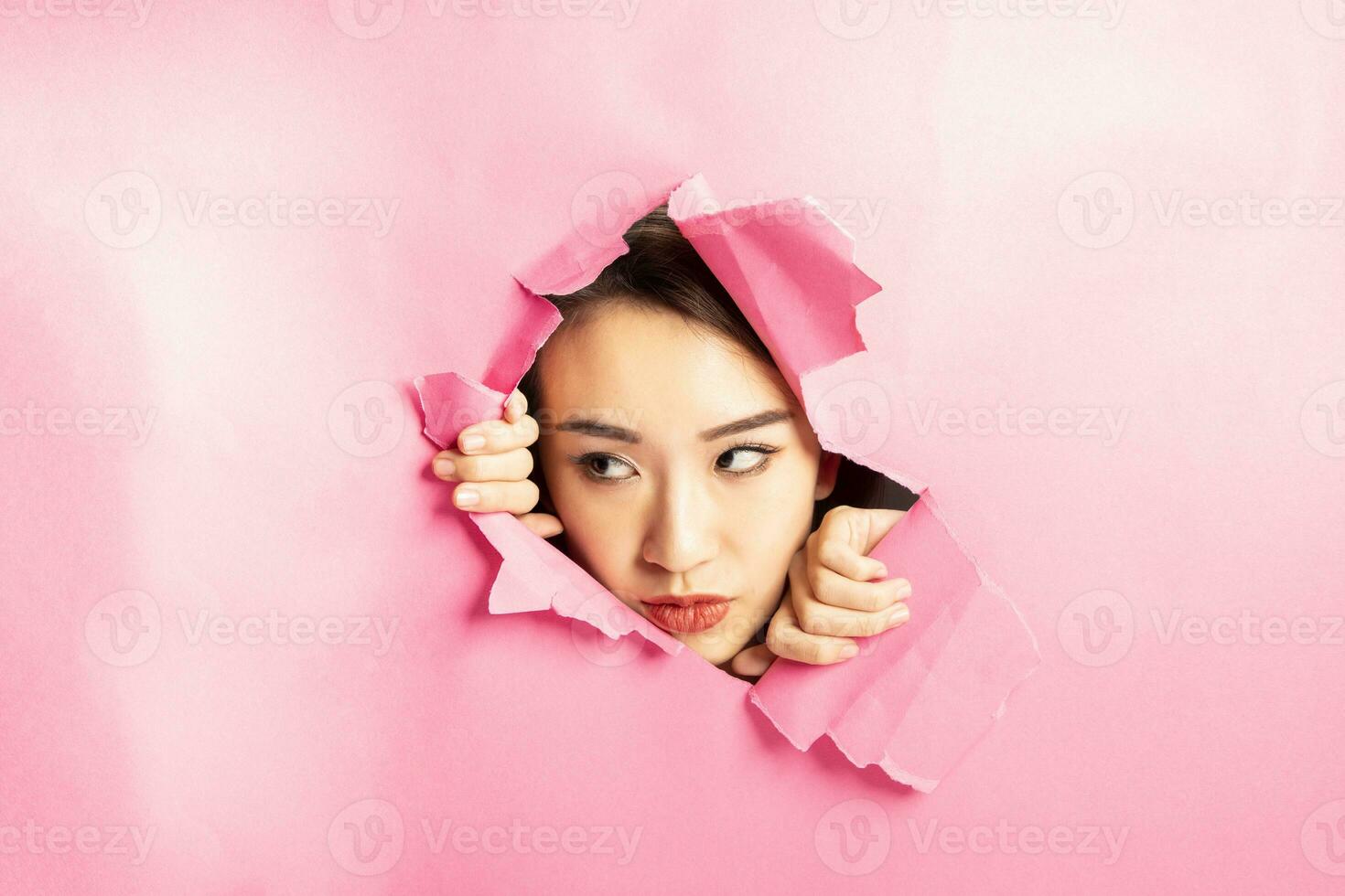 Young beautiful Asian woman expression through torn paper hole photo