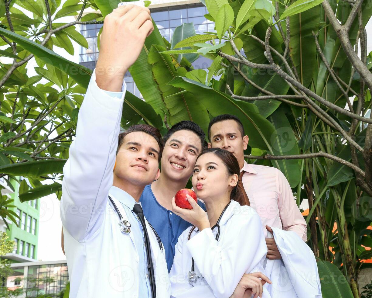 South East Asian young Malay Chinese man woman medical doctor group holding smart phone taking selfie self portrait photo