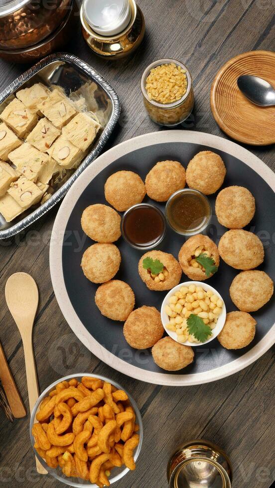 verity of indian bengali street food tea time snacks onion pakoda crunchy spicy lentils moong dal fry sweet shompapri chaat pani puri fuska on rustic retro table plate brass copper pots silver tray photo