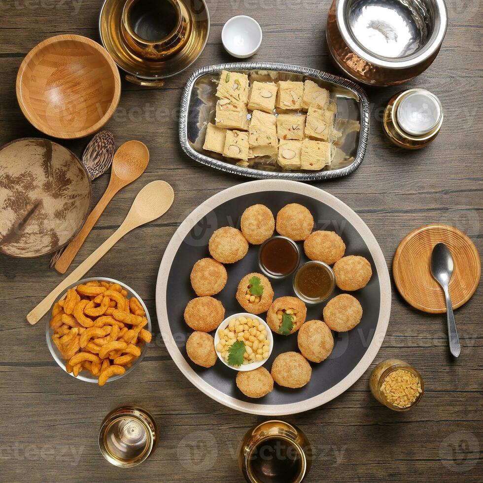 verity of indian bengali street food tea time snacks onion pakoda crunchy spicy lentils moong dal fry sweet shompapri chaat pani puri fuska on rustic retro table plate brass copper pots silver tray photo