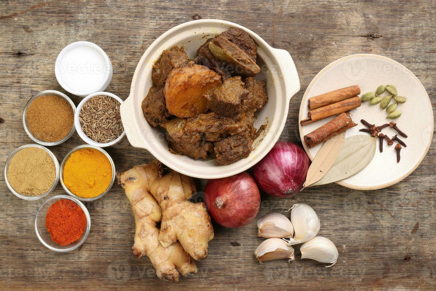 Beef bhuna dry curry with potato in ceramic bowl ingredients chilli cumin coriander turmeric powered salt onion garlic ginger bay leaf cinnamon cardamom clove over rustic wood background photo