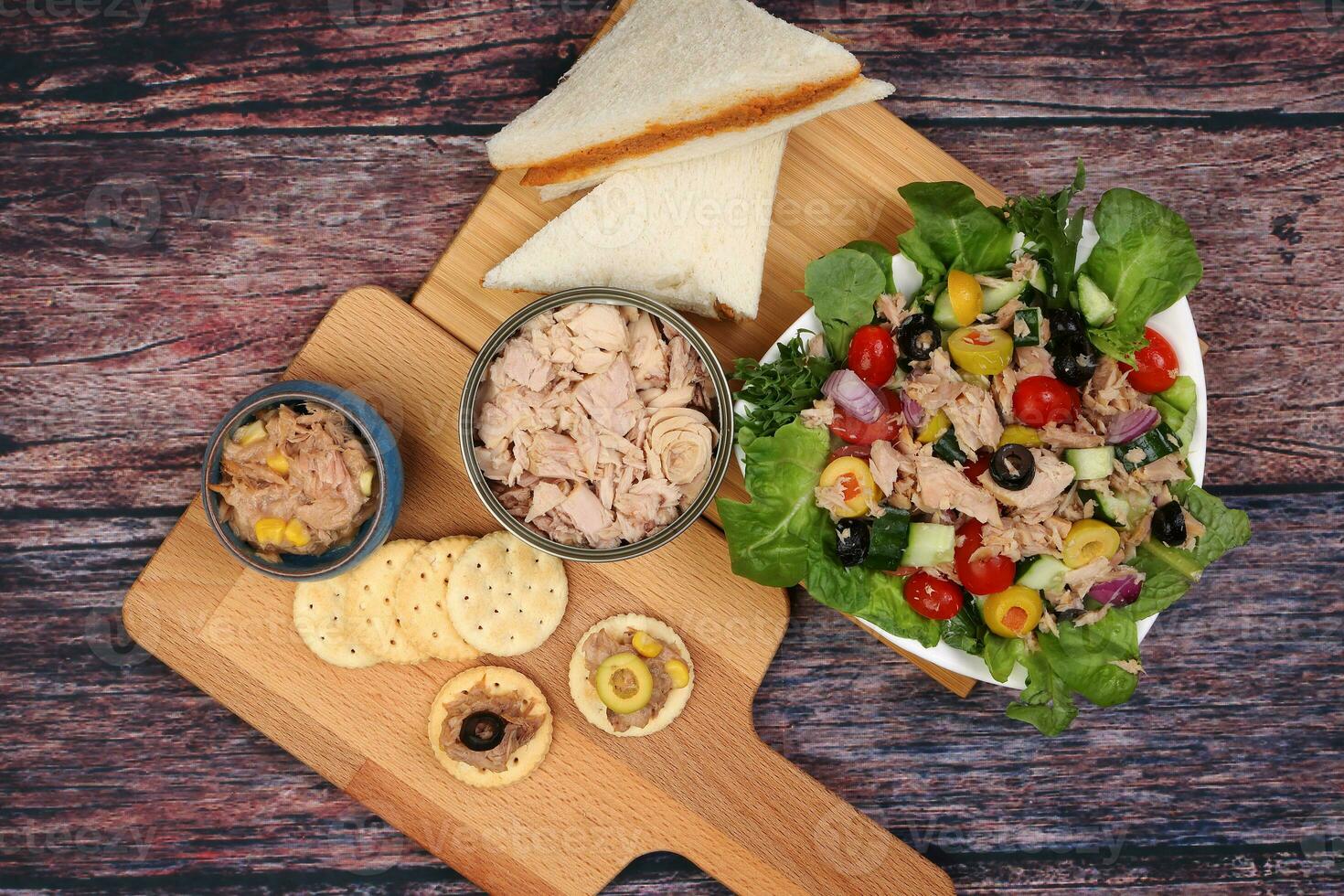 Tin can tuna fish meat chunk flake product recipes salad spread topping tapas cracker sandwich on wooden black slate board over rustic wooden table photo