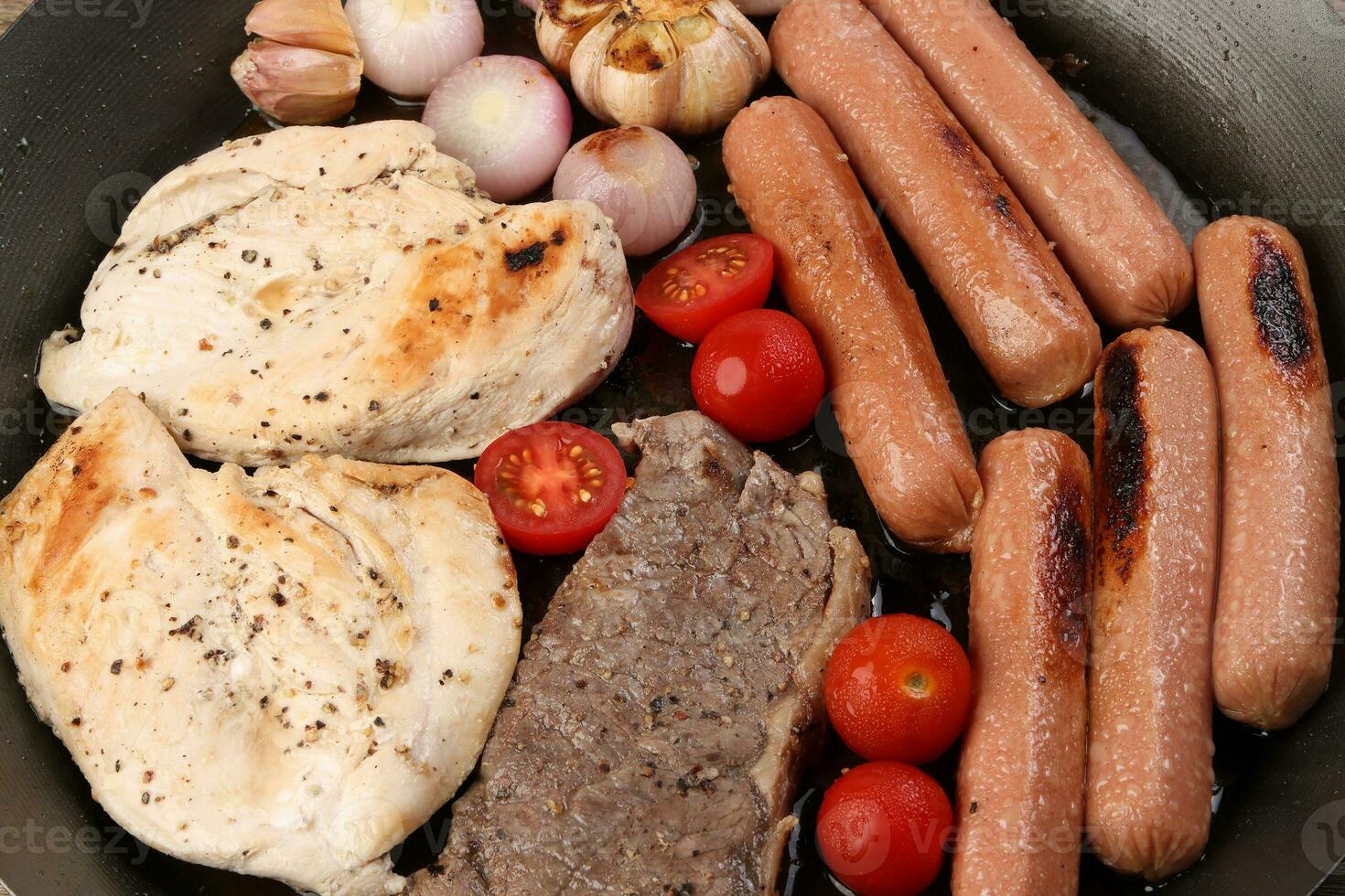 Mix meet pan chicken breast beef steak sausage tomato onion garlic oil fry grill on metal frying pan two wooden handle on white background photo