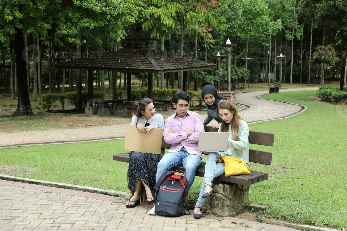 Young asian malay chinese man woman outdoor on park bench study talk discuss point laptop file book photo