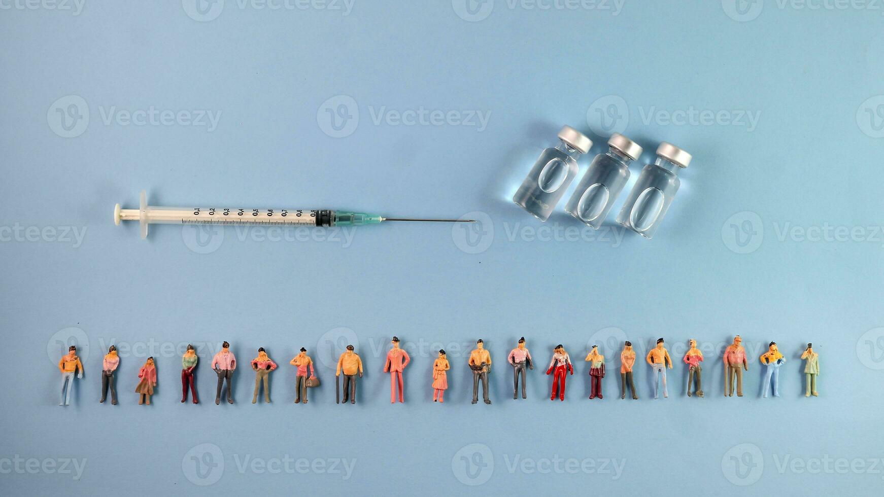 Miniature human figure figurine male female doll row line vaccine bottle medical injection syringe needle border copy text sign space on blue paper background photo