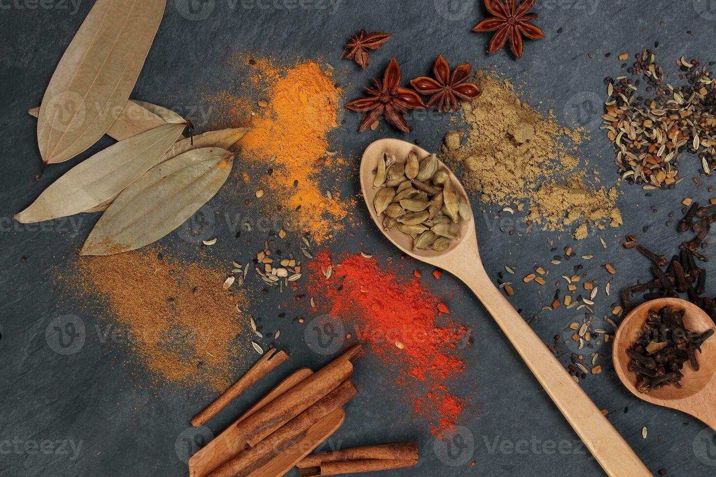 Mix variety spice cinnamon cardamom clove bay leaf wooden chilli cumin turmeric powered on black slate background photo