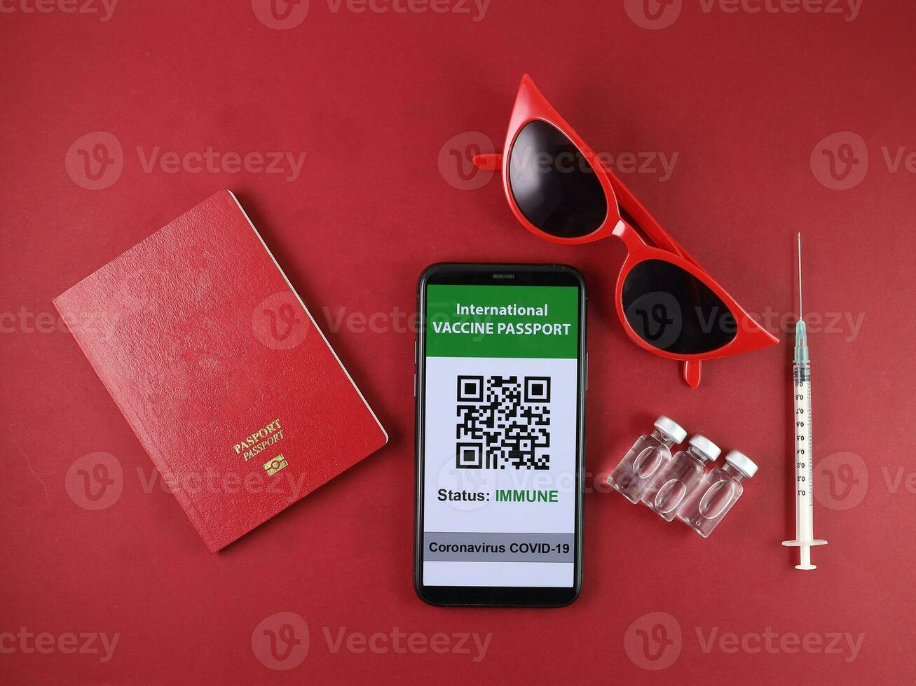 Red eyewear sunglass vaccine passport smartphone book injection bottle medical syringe needle travel vacation red paper background photo