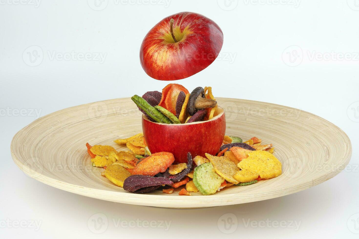 Healthy vegetable chips yellow sweet potato purple carrot green radish green beans and shiitake mushrooms in hollow red apple white background wooden plate photo
