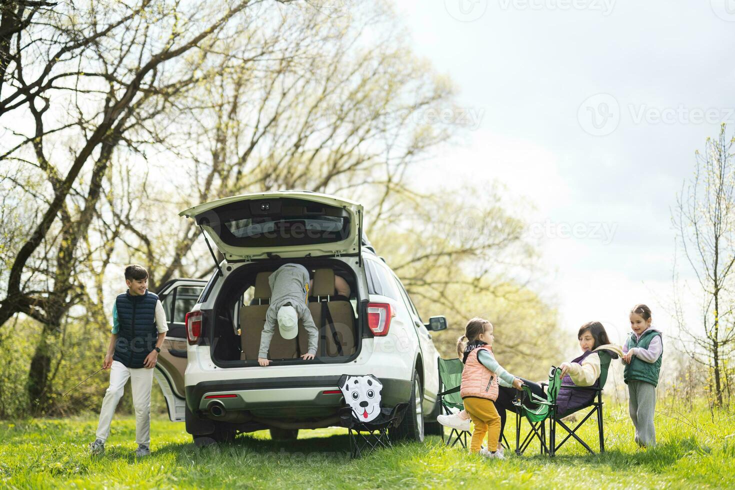madre con niños sentar en silla en contra coche abierto maletero en picnic. foto
