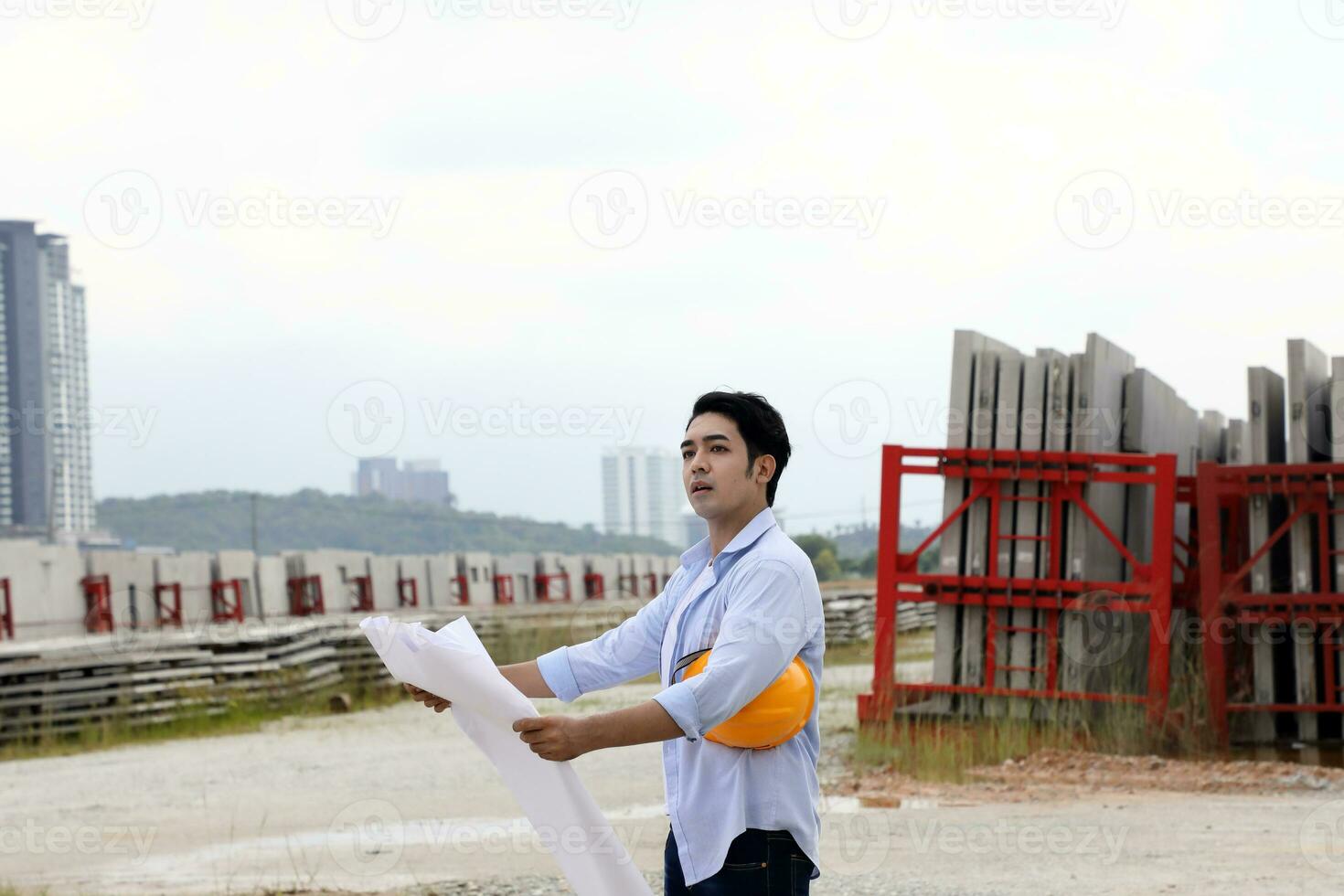 Asian man malay worker engineer management hard safety hat helmet at construction site reading seeing plan blue sky photo