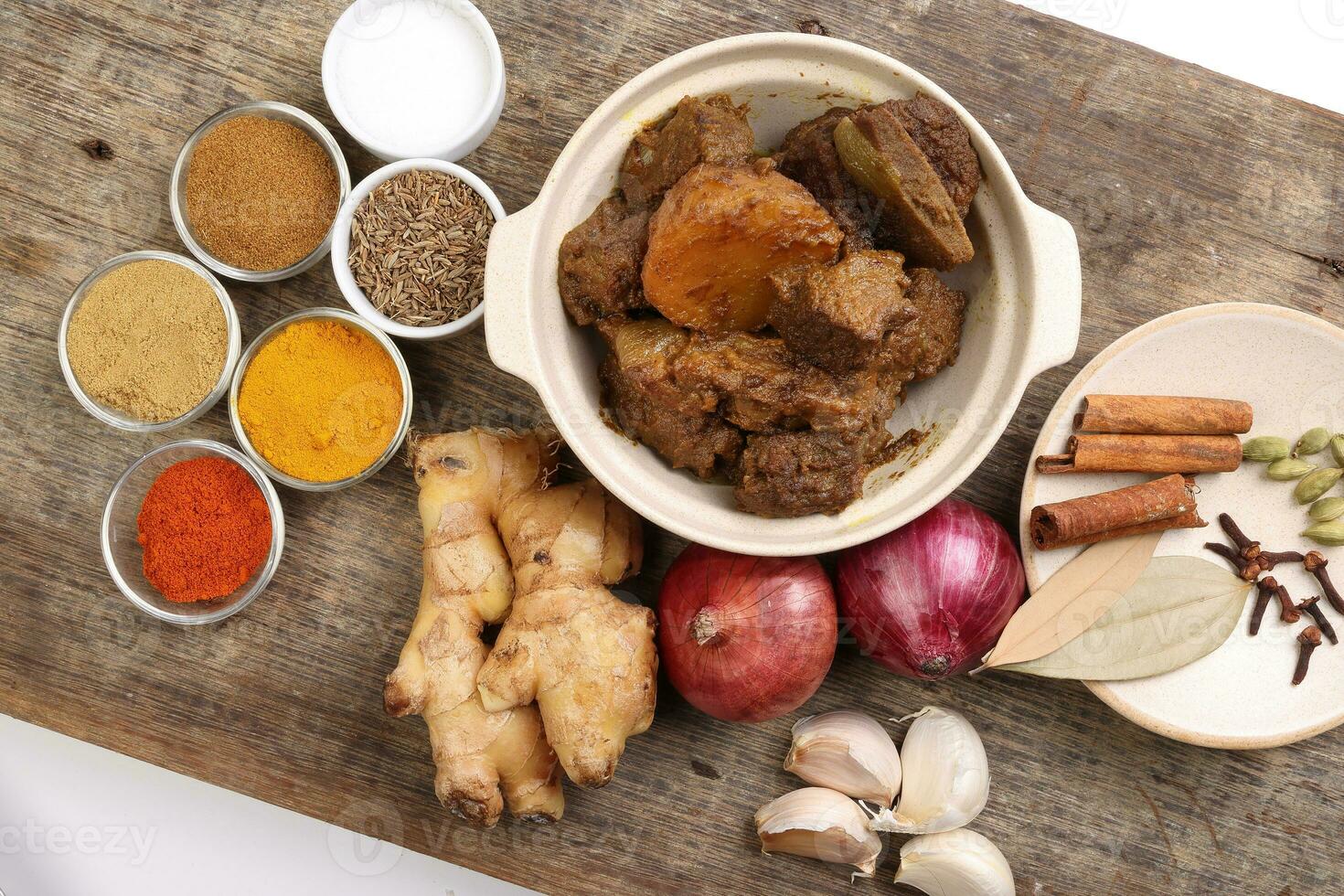 Beef bhuna dry curry with potato in ceramic bowl ingredients chilli cumin coriander turmeric powered salt onion garlic ginger bay leaf cinnamon cardamom clove over rustic wood background photo