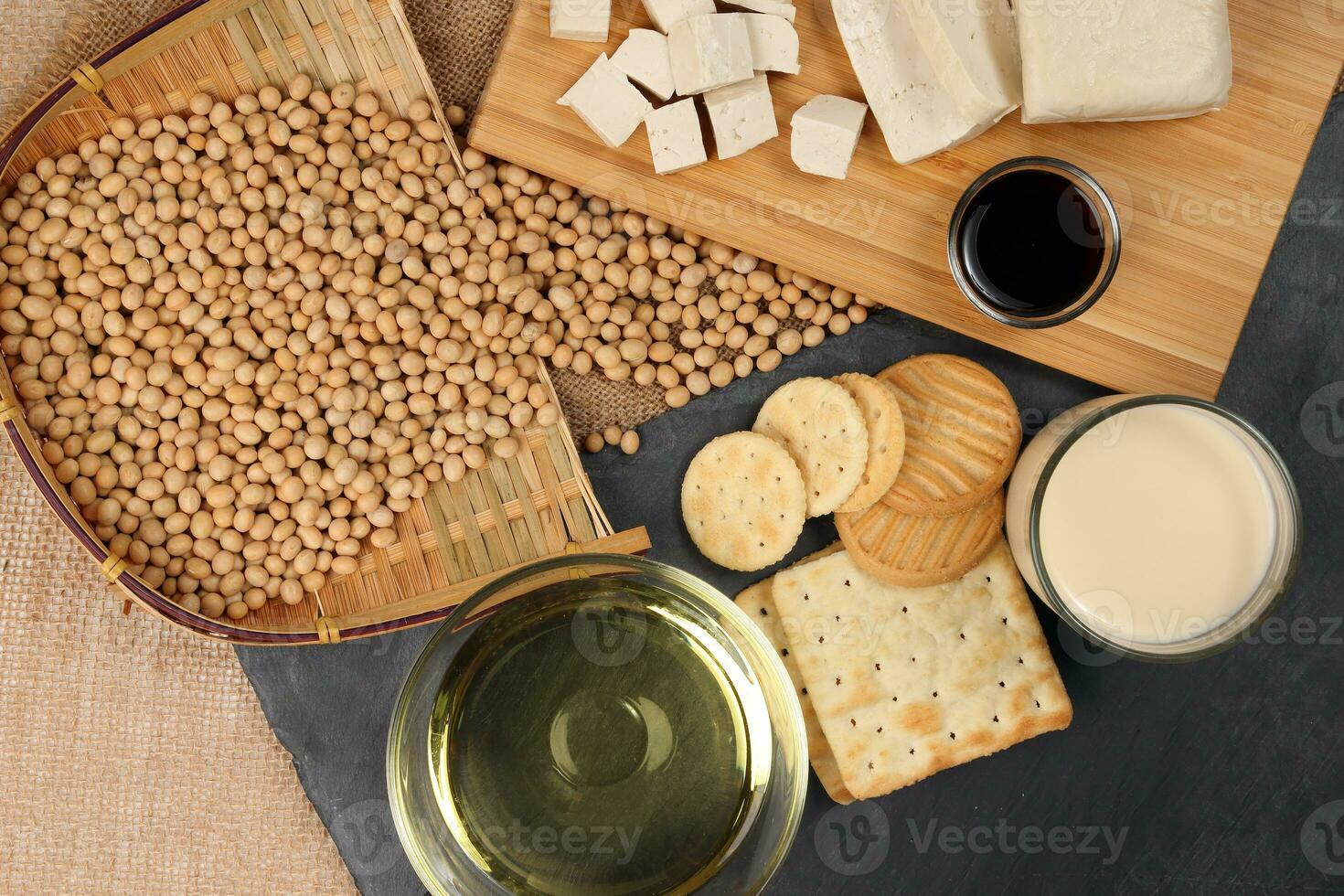 Soyabeans products soya beans flowing bamboo sieve wooden board on jute black stone slate background curd tofu oil milk sauce biscuit cookies photo
