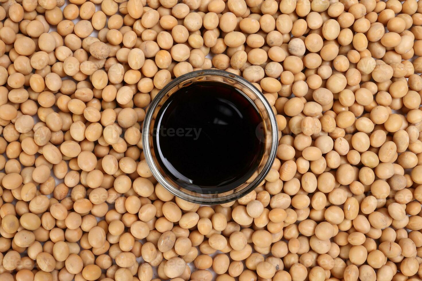 Soya sauce in small glass bowl on bed of soyabean background photo