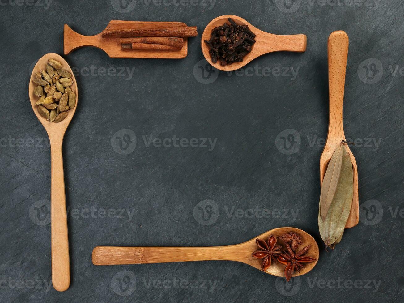 Mix variety spice cinnamon cardamom clove bay leaf wooden spoon border frame copy text space on black slate background photo