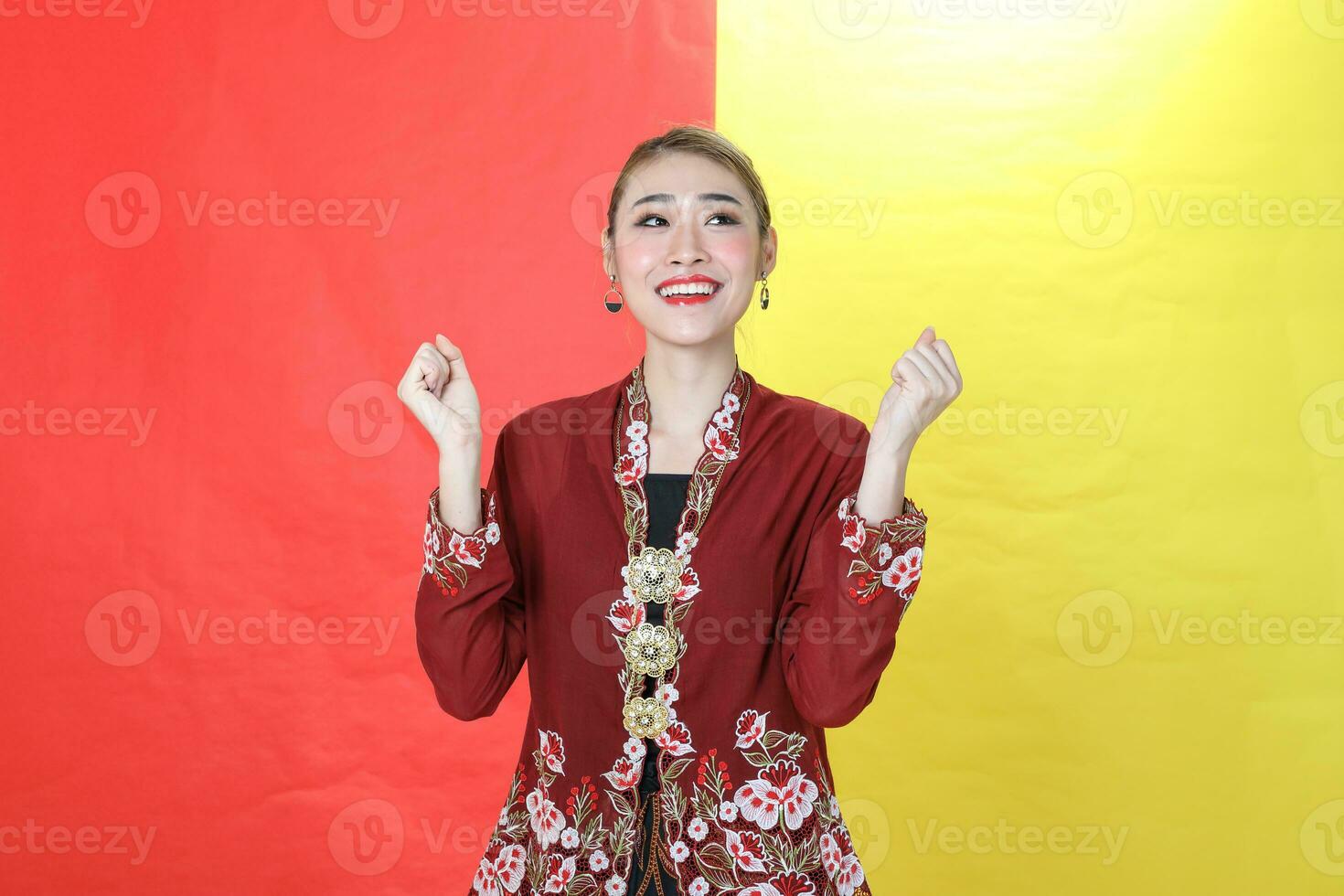 asiático mujer tradicional granate kebaya compartir en rojo amarillo papel antecedentes posando contento éxito puño en aire foto