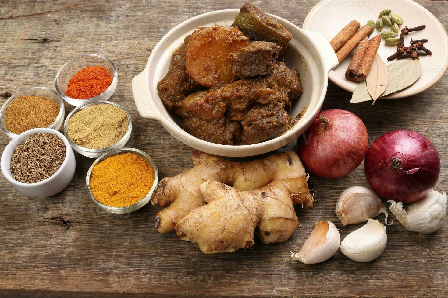 Beef bhuna dry curry with potato in ceramic bowl ingredients chilli cumin coriander turmeric powered salt onion garlic ginger bay leaf cinnamon cardamom clove over rustic wood background photo