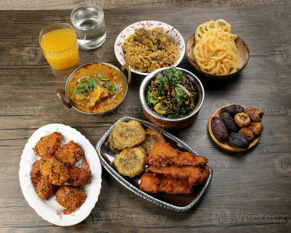Bengali Iftar Ramadan breakfast spread ripe dates peep fried spicy piaju onion fitter eggplant tanpura potato chop haleem jilapi khichuri rice chana sola curry on rustic wooden table photo