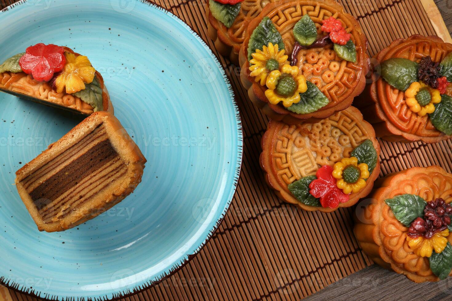 Colourful flower decorated mooncake Chinese mid autumn festival cut slice on blue ceramic plate background on bamboo food mat photo