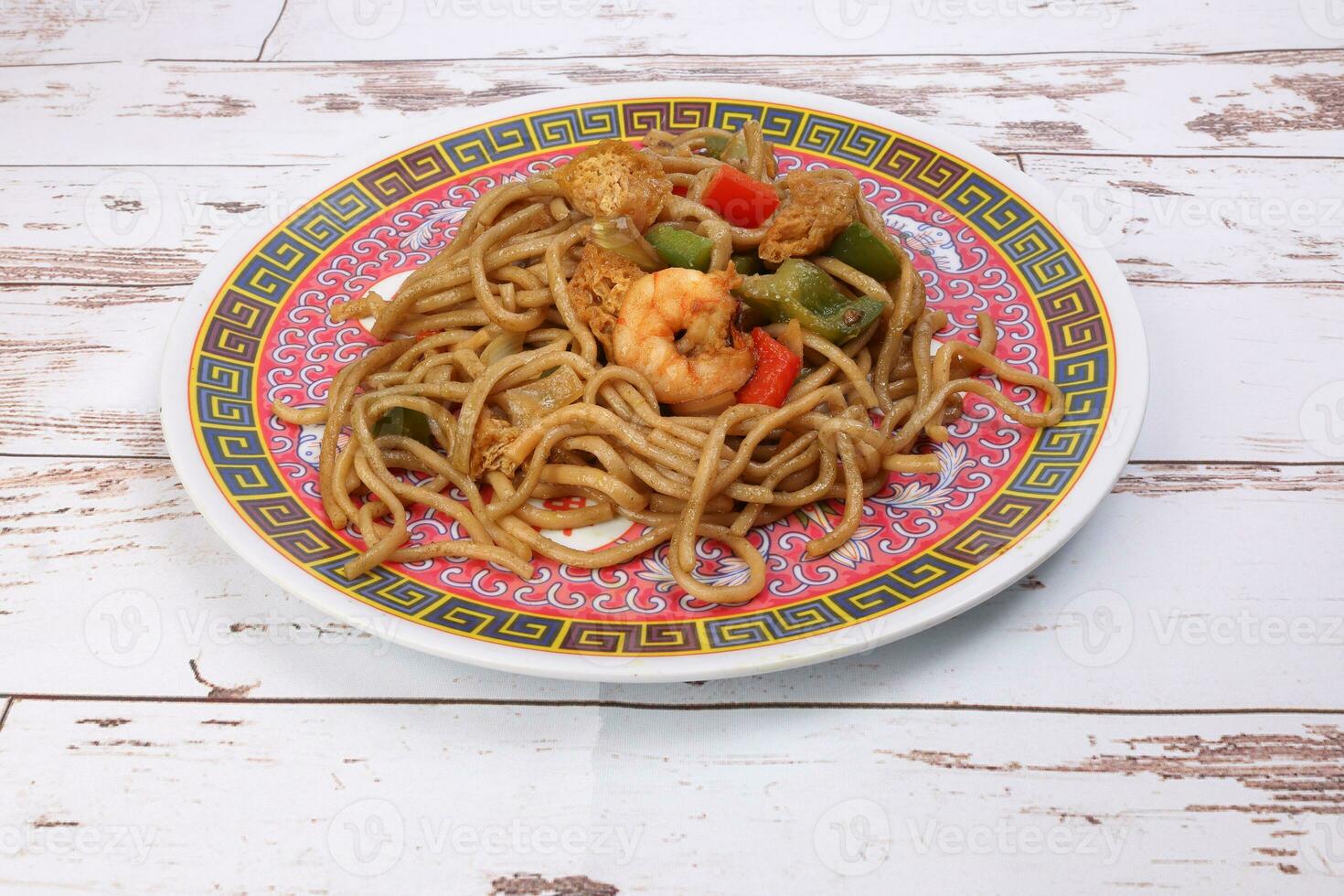 Stair fried noodle with prawn seafood tofu colorful pepper on oriental style plate over rustic wooden background photo