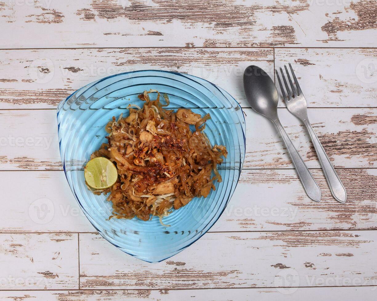 Thai style stair fried flat rice noodles pad thai on a blue glass triangular plate fork spoon on rustic wooden background photo