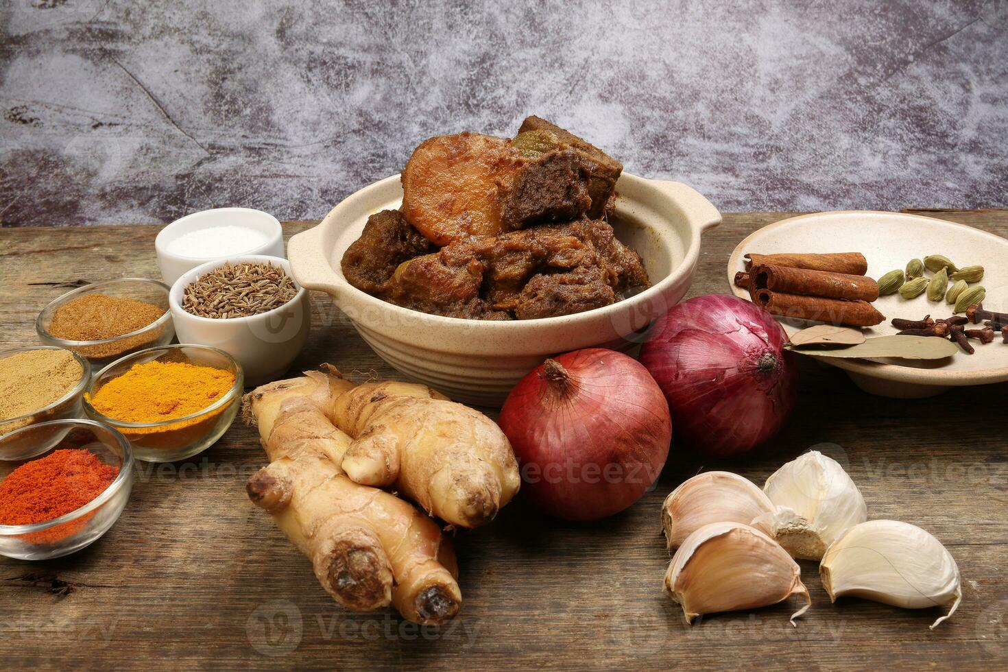 Beef bhuna dry curry with potato in ceramic bowl ingredients chilli cumin coriander turmeric powered salt onion garlic ginger bay leaf cinnamon cardamom clove over rustic wood background photo
