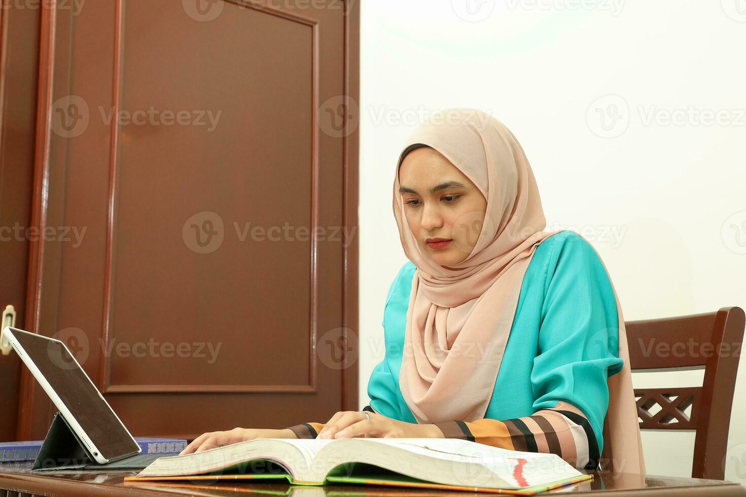 young Asian Malay muslim woman wearing headscarf at home office student sit at table computer read book file paper study work photo