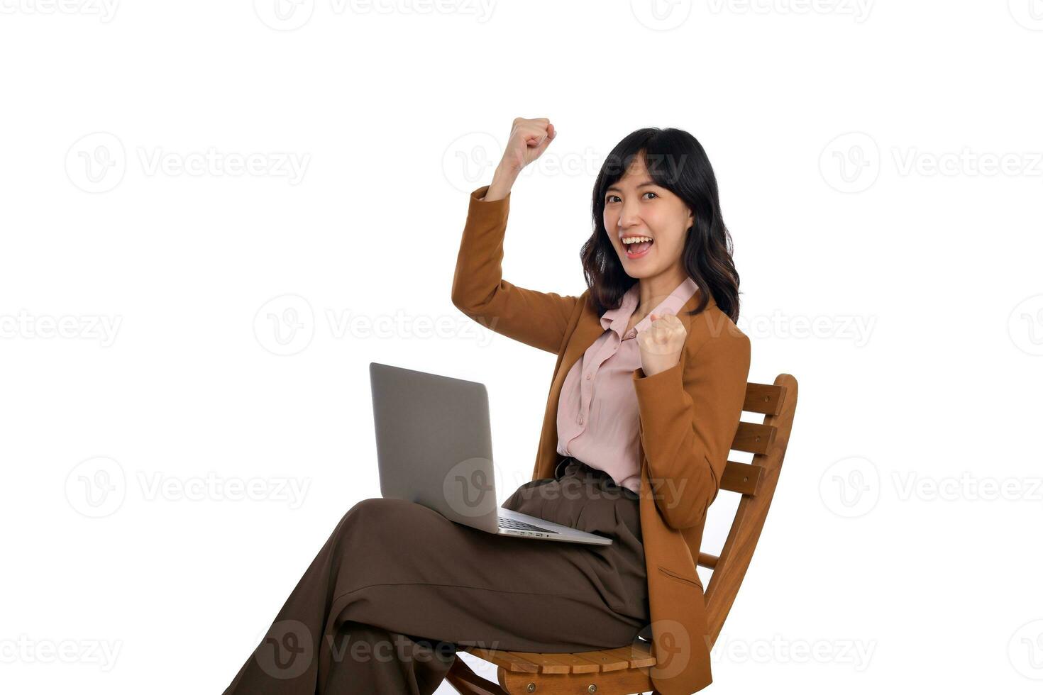 contento joven negocio asiático mujer celebrando en su éxito. mientras su utilizando ordenador portátil sentado en de madera silla aislar en blanco antecedentes foto