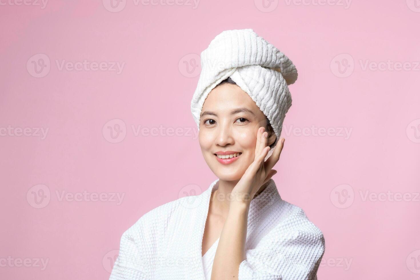 Beautiful young asian woman happy with clean face skin in towel and bathrobe, spa suit on pink background. Skincare, treatment, wellness therapy, facial care, beauty female health, cosmetology concept photo