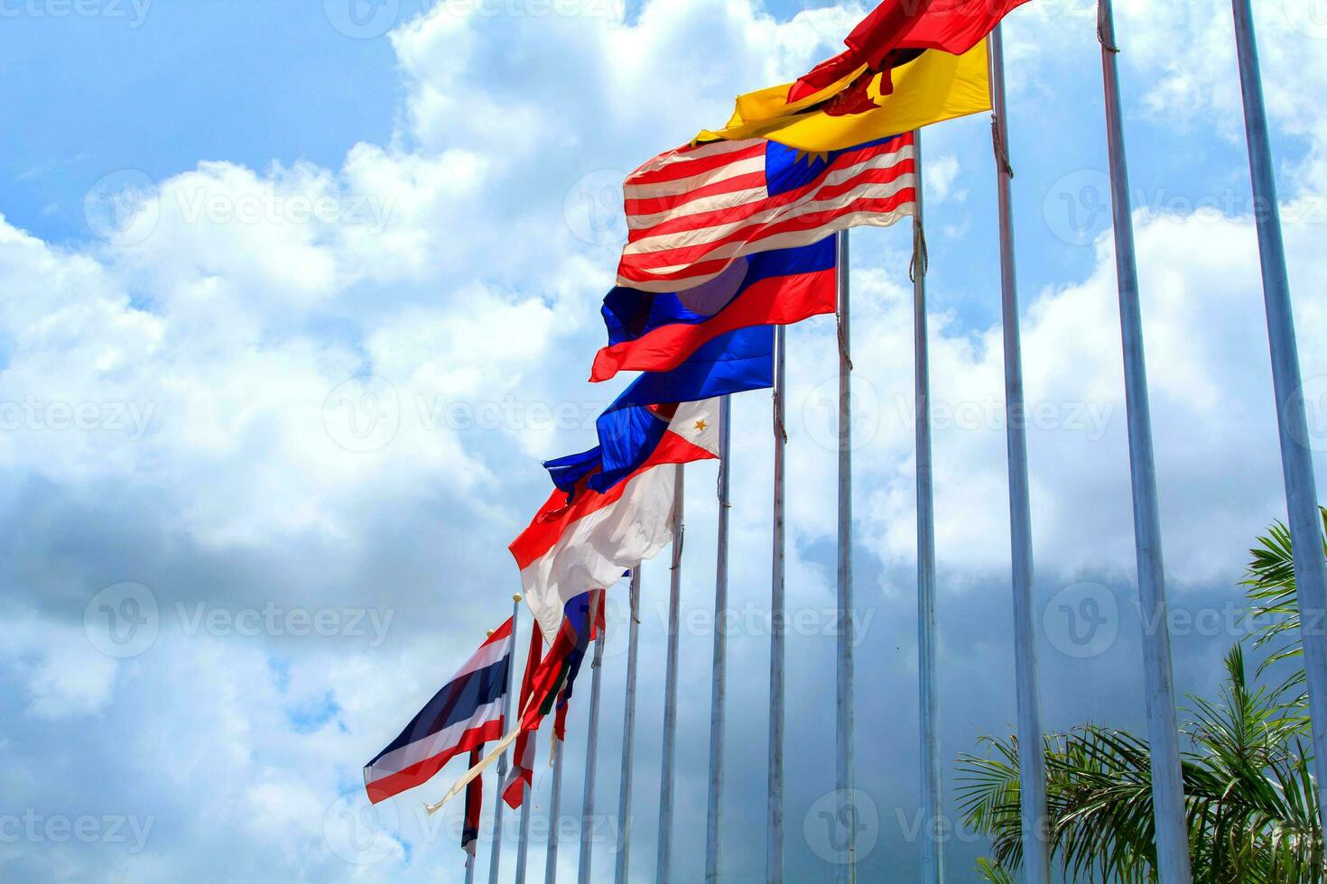 Many of the flags of ASEAN in the colorful colors blown by the force of the wind fluttering on a pole in front of a hotel in Thailand on a background with clouds and blue skies. photo