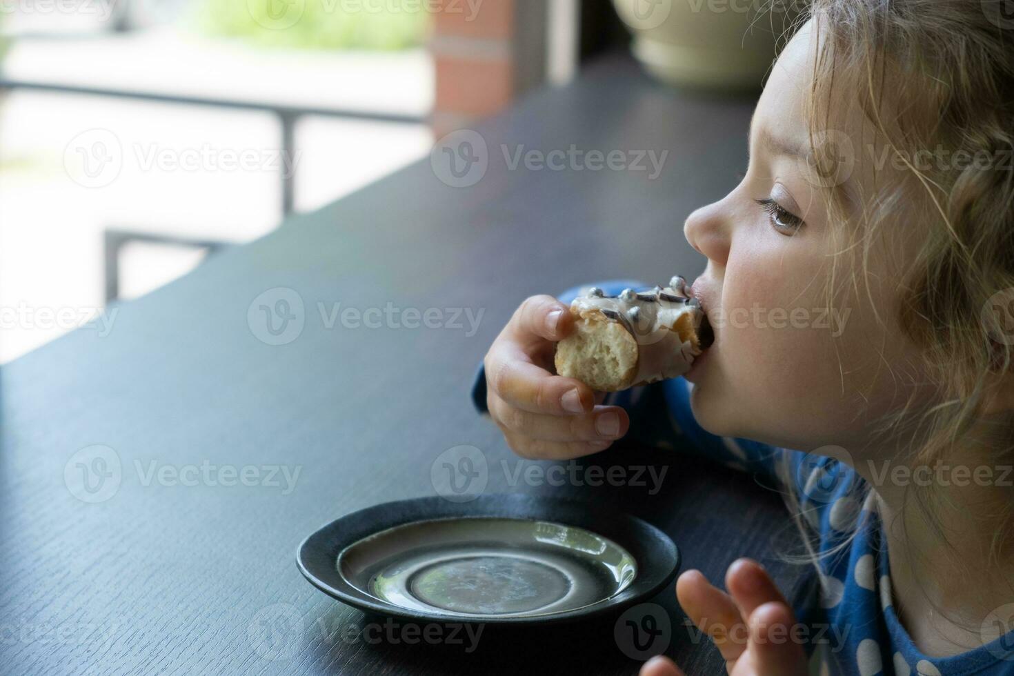 A little girl eats a donut in a cafe. Enjoying sweet food photo