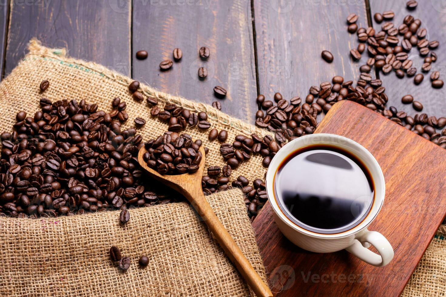 Freshly brewed coffee. Coffee cup or mug arranged on a black wooden table with roasted coffee beans. Espresso mocha cappuccino barista on dark background - top view photo