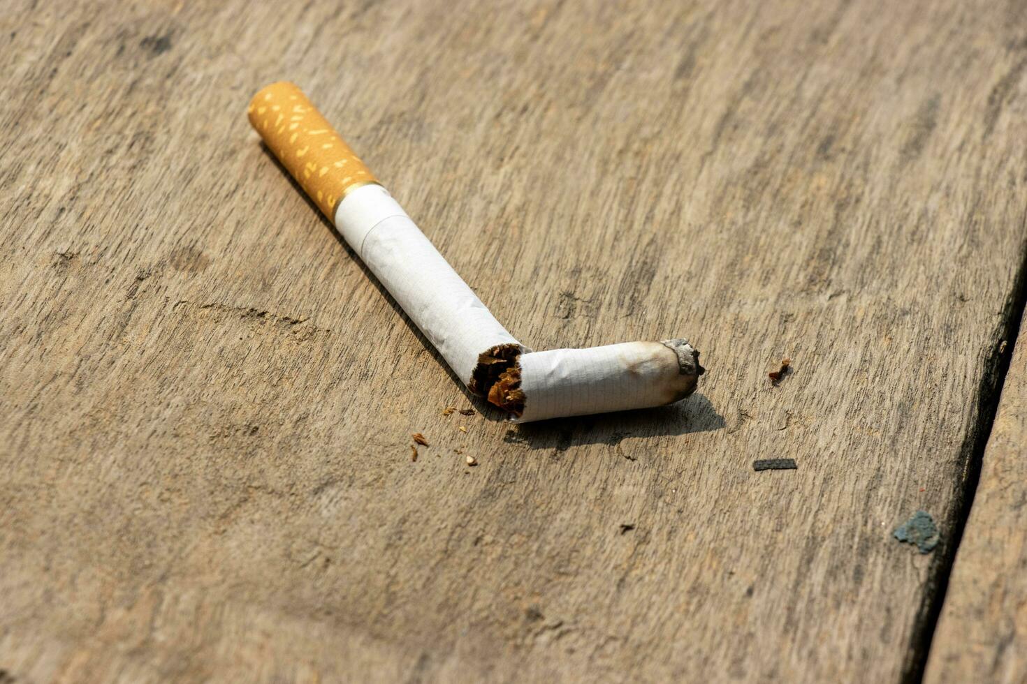 Broken cigarette on a wooden table close up shot. No smoking and ban cigarette concept with a broken cigarette. A broken cigarette on a wooden surface with tobacco powder around it. Burned cigarette. photo