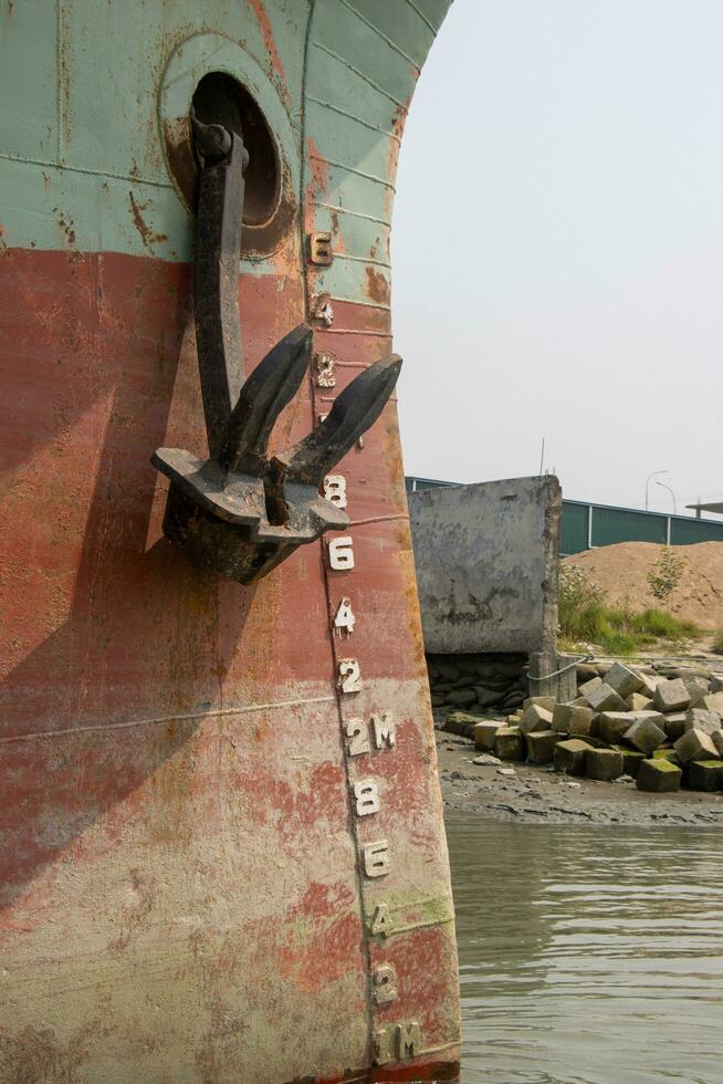 Ship with anchor and rusty metal body on a riverbank. Rusty cargo ship with water meters in front of it. Old waterway vessel and tanker ship on a river. Water transportation and logistics concept. photo