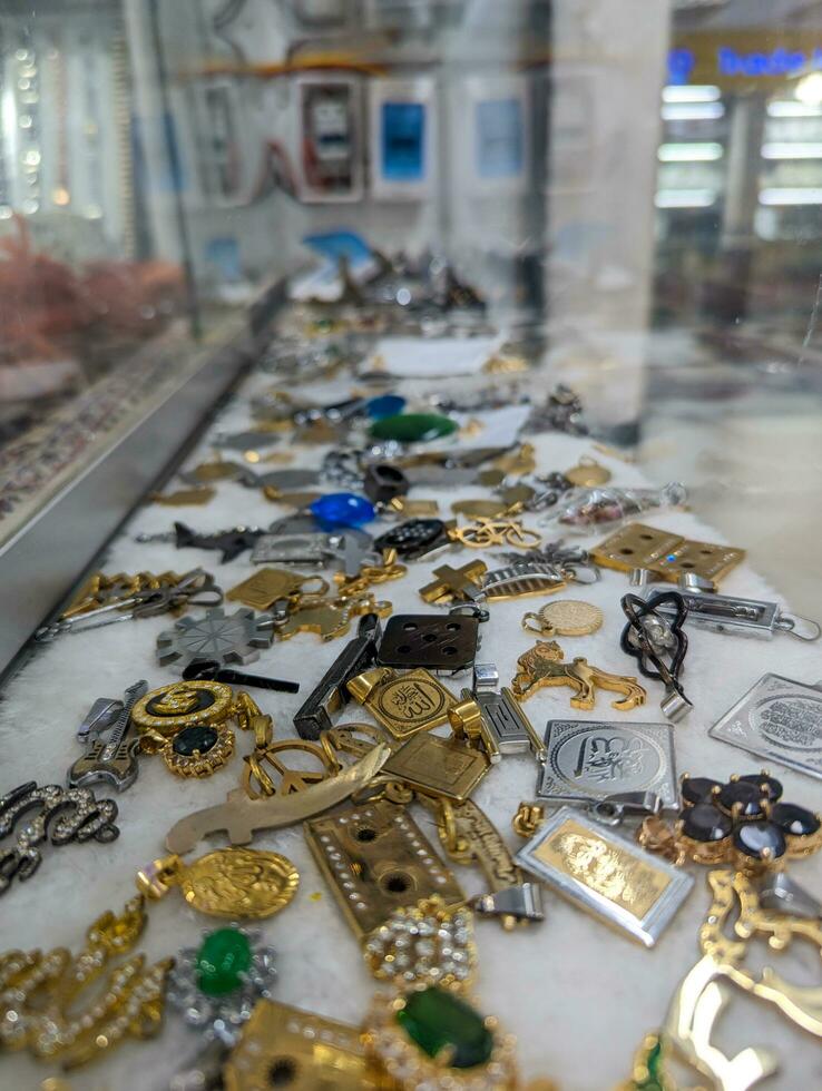 Silver and gold jewelry for men. Metal jewelry in a showcase. Male keyrings and lockets in the market. Colorful and stylish male jewelry on a Southeast Asian market. Stylish key rings and lockets show photo