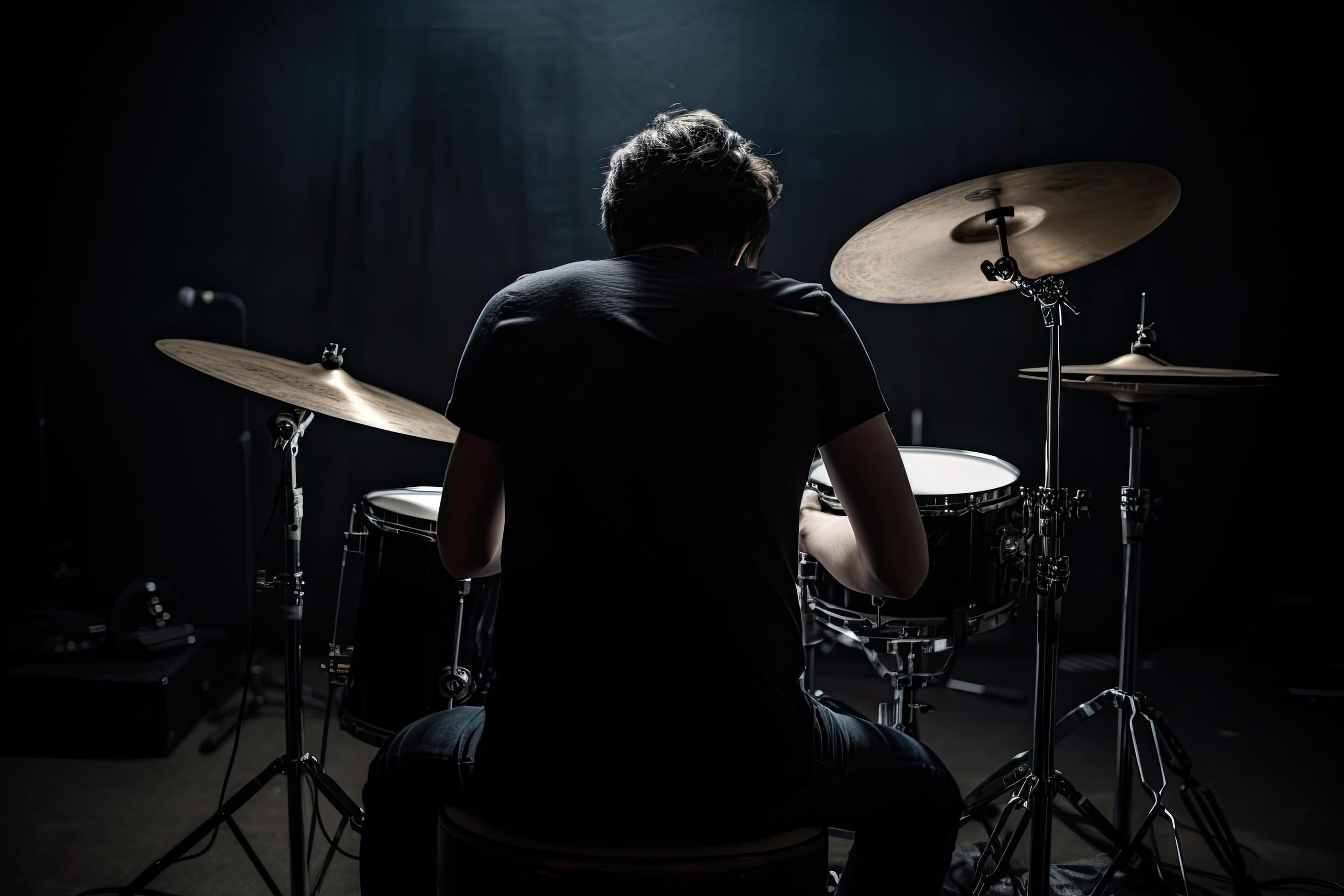 Young man playing drums on a stage in a dark room with dramatic