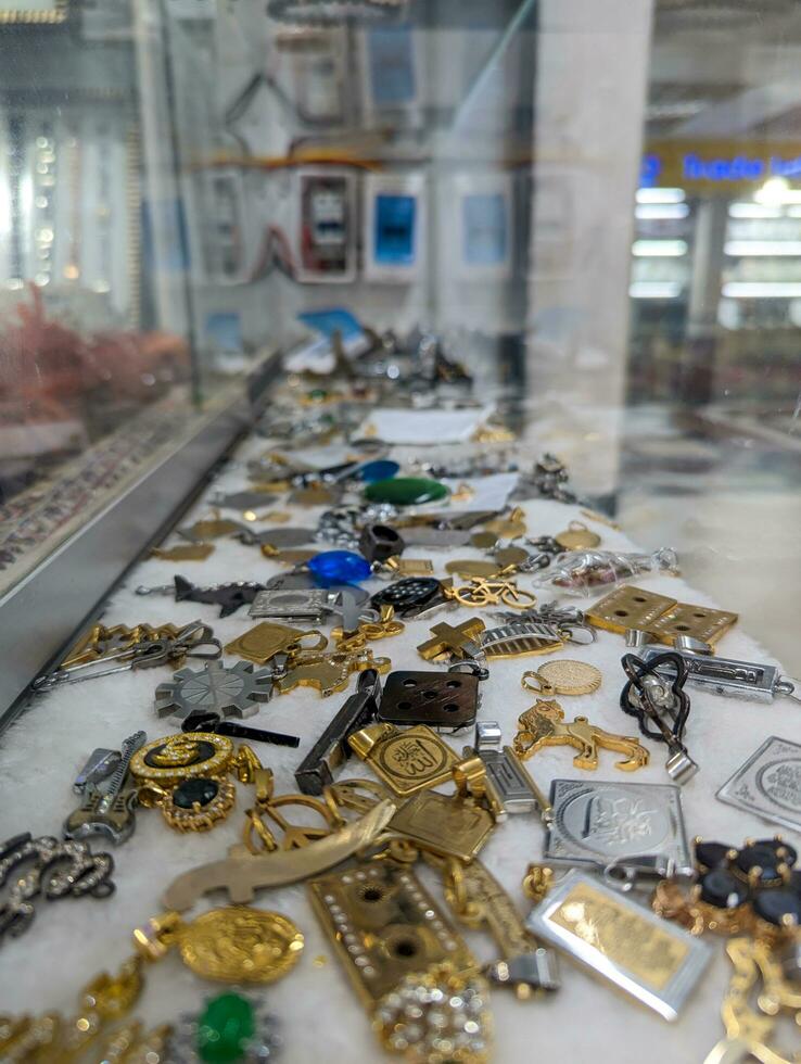 metal joyería en un escaparate. masculino llaveros y medallones en el mercado. elegante llave anillos y medallones espectáculo. vistoso y elegante masculino joyería en un Sureste asiático mercado. plata y oro joyería para hombres foto