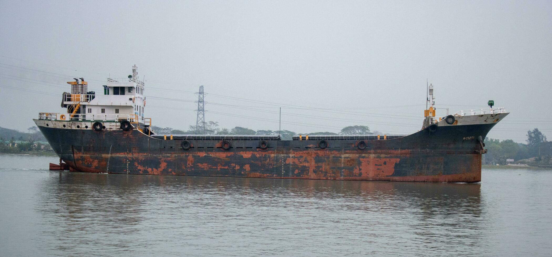 Old and rusty cargo ship full body side view. Water transportation and logistics concept. Cargo ship with rusty metal anchors going through a river. Old waterway vessel and tanker ship on a river. photo