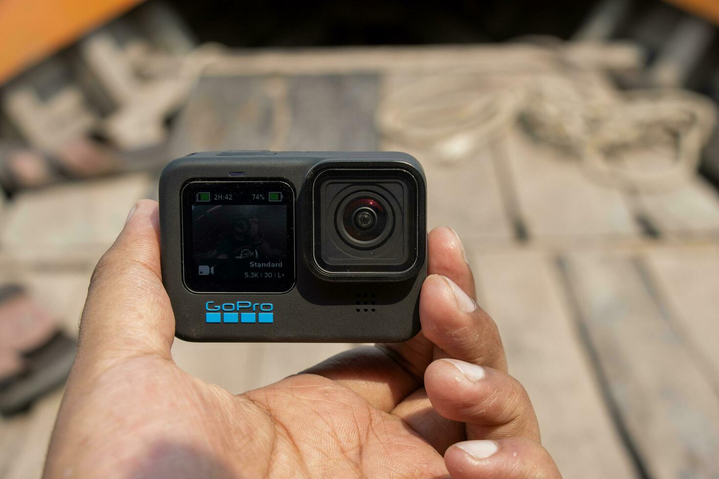 Barisal, Bangladesh - March 12, 2023, Modern action camera close up shot on hand and a blurry wooden boat. GoPro 11 action and video cam with a black body. Professional action camera on hand. photo