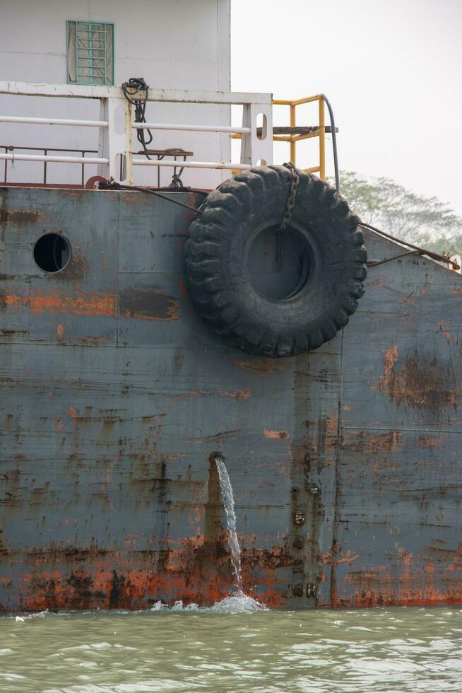 Old and rusty cargo ship side view. Old waterway vessel and tanker ship on a river. Ship with tire and rusty metal body going through a river. Water transportation and logistics concept on a canal. photo