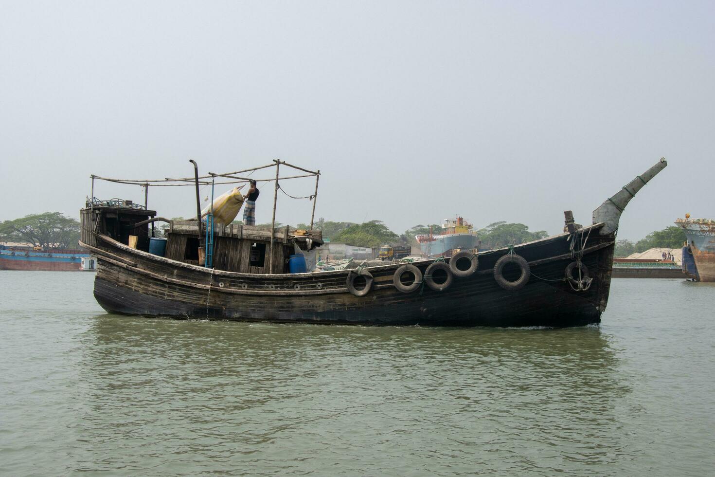 Southeast Asian fisher boat running through a river. Old wooden fishing trawler side view. Beautiful rural life and waterway transportation concept. Wooden boat going through a canal. photo