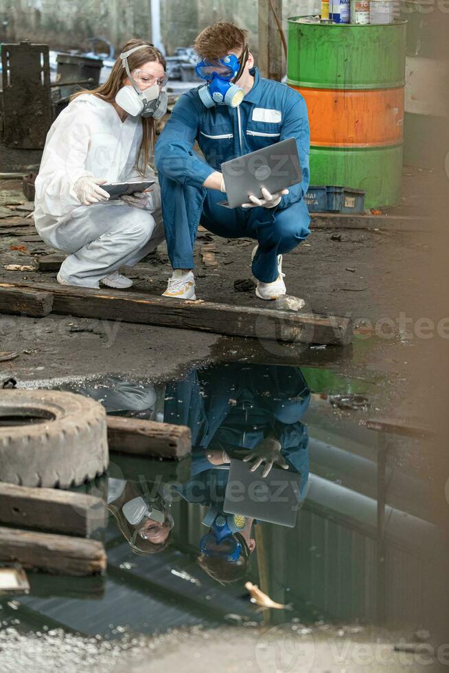 emergency pollution factory concept. engineers wearing mechanic jumpsuits and ppe and gas masks inspect oil on the factory floor. photo