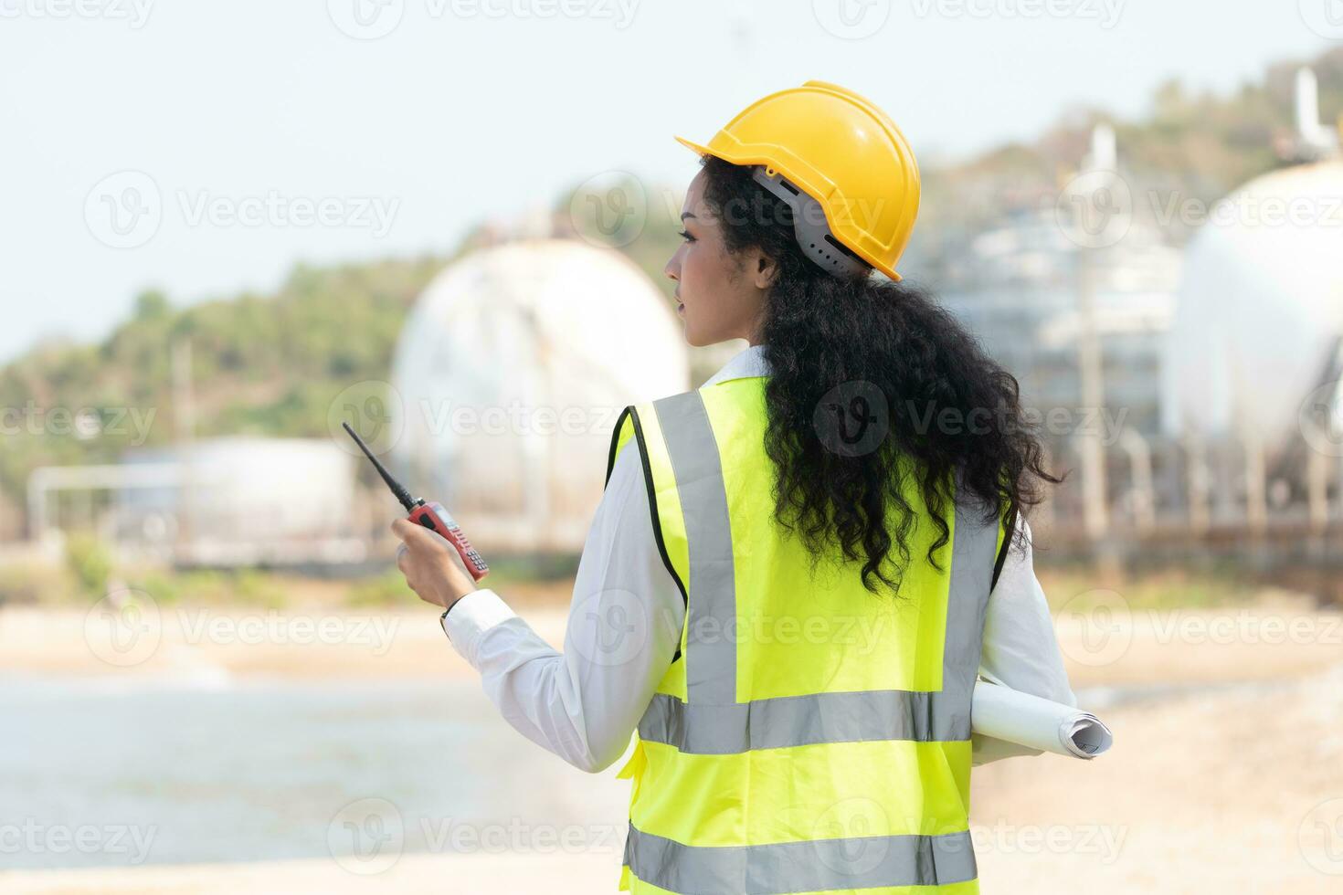 female engineer with hardhat with petrochemical factory background. asian woman holding tablet, plan and Walkie Talkie. photo