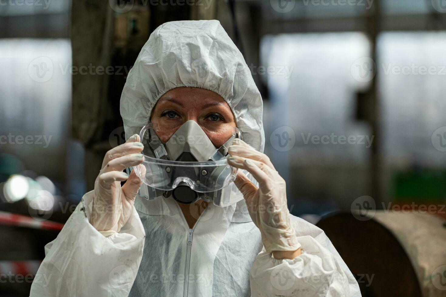 Caucasian woman workers wearing PPE protective clothing and gas masks, goggles, holding old petrol tanks. photo