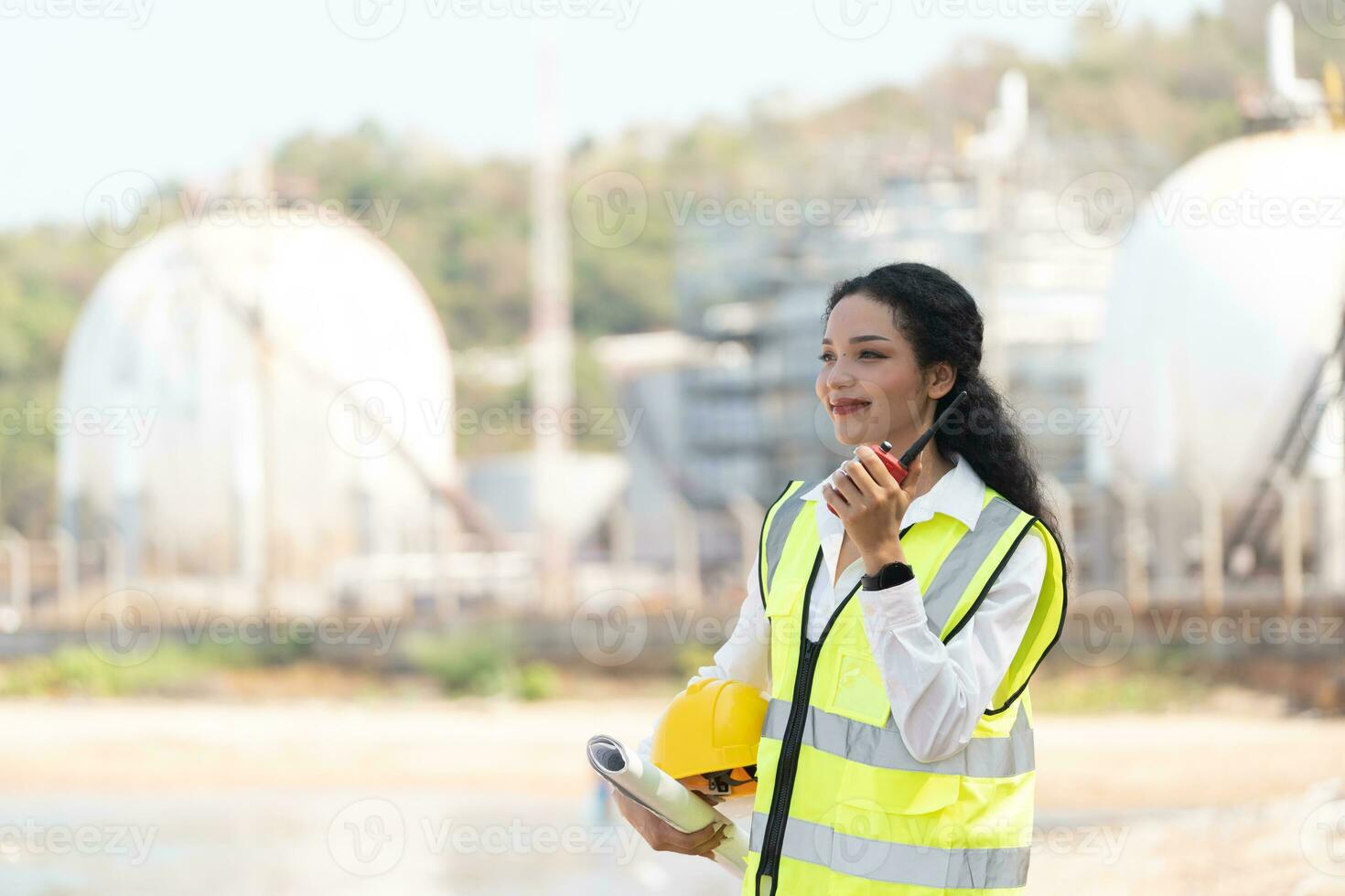 female engineer with hardhat with petrochemical factory background. asian woman holding tablet, plan and Walkie Talkie. photo